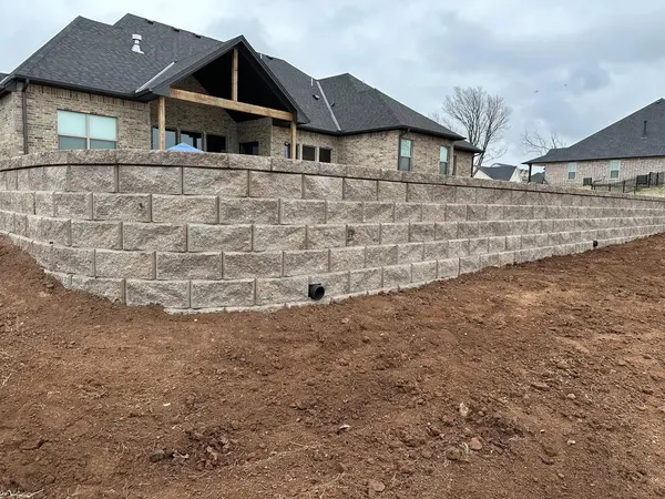 Tall curved segmental block retaining wall with drain outlets wrapping a new home