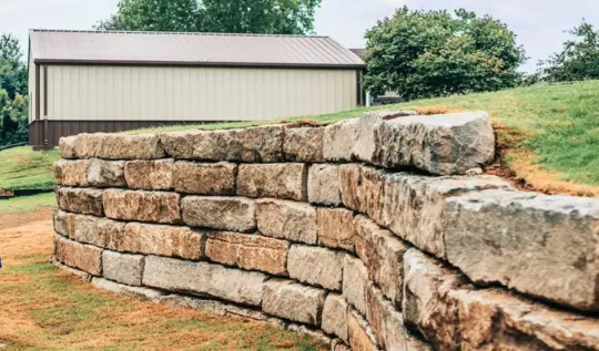 Stacked natural stone boulder retaining wall holding a grass slope