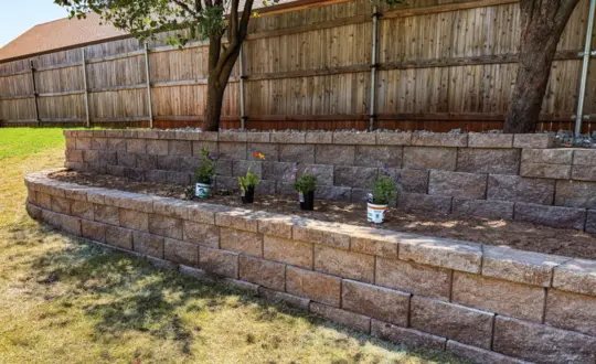 Two-tier block garden wall planter bed with fresh flowers along a fence line