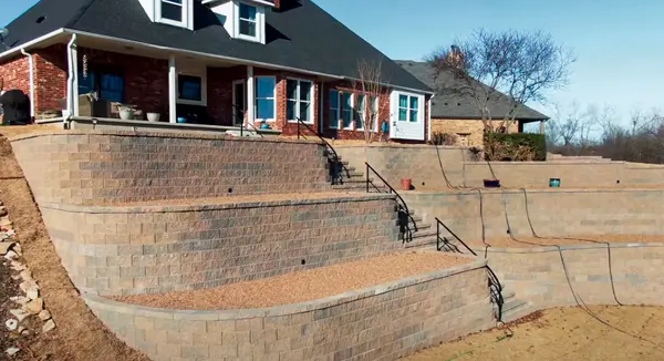 Curved multi-tier retaining wall terraces with block stairs and railings behind a brick home