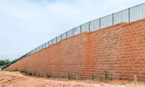 Tall subdivision perimeter retaining wall with metal fence running along the top