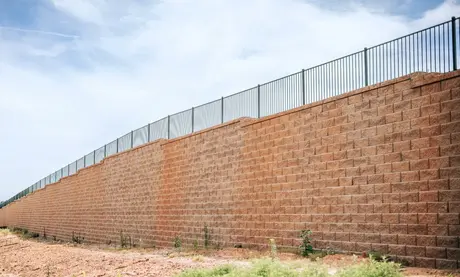 Tall segmental block retaining wall with a metal fence along the top