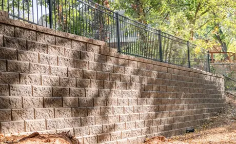 Close-up of a textured segmental block retaining wall with a black metal railing along the top