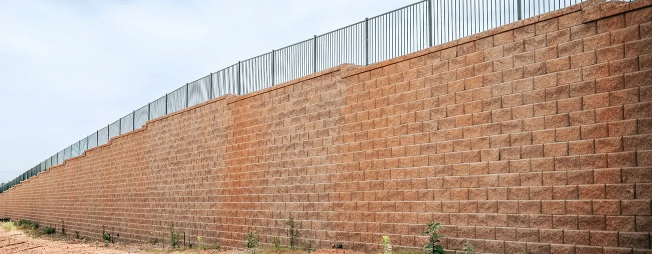 Tall block retaining wall with metal fence running along the top of a development