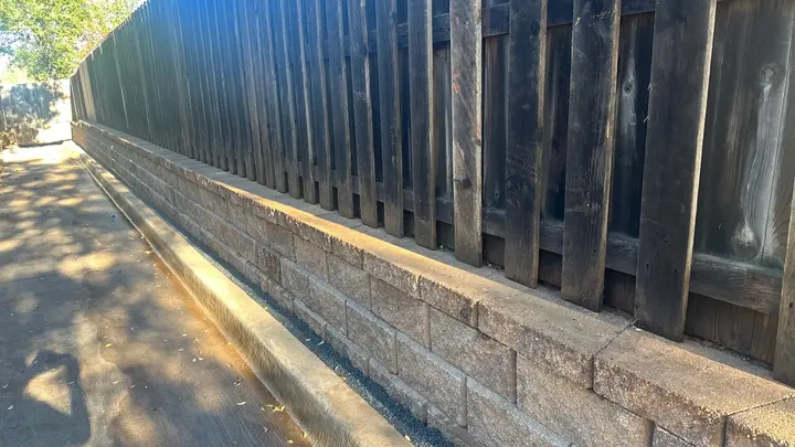 Long block retaining wall running between a fence and a concrete drainage path