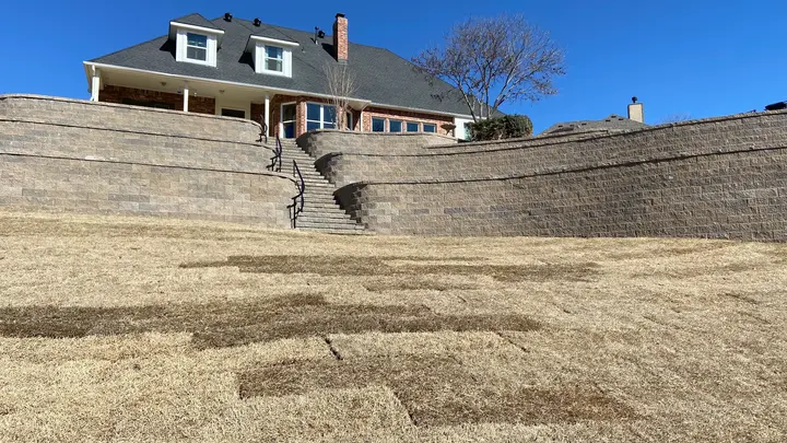 Completed multi-tier retaining wall terraces with block stairs and metal railing on a steep backyard hill