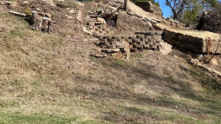 Collapsed sections of an old block retaining wall on a bare slope before rebuild