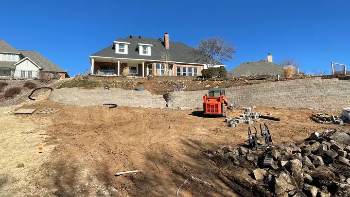 Skid steer and block materials staged below a new retaining wall under construction