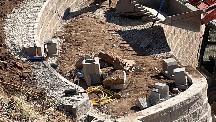 Curved retaining wall courses under construction with gravel backfill and geogrid