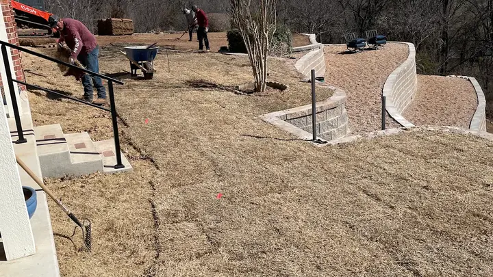 Crew laying fresh sod around new curved retaining walls on a hillside