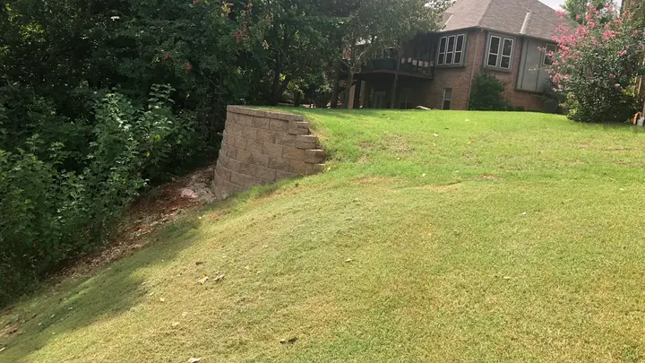 Small curved retaining wall at the edge of a backyard drainage swale