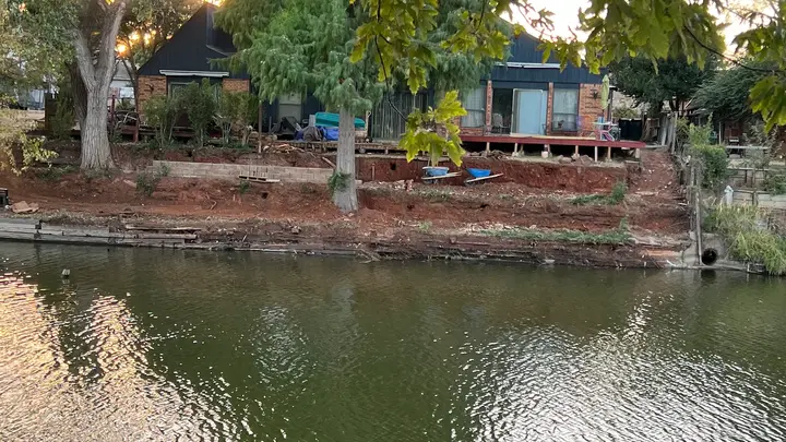 Eroded pond bank with failing timber walls before the retaining wall rebuild