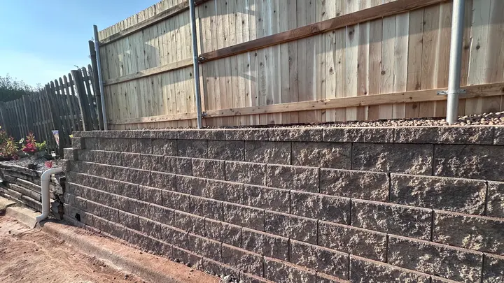 Textured block retaining wall with a drainage outlet at the base and a new cedar fence above