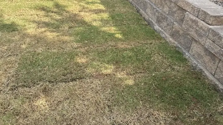 Two-tier block retaining wall with a river rock bed beneath a fence line and fresh sod