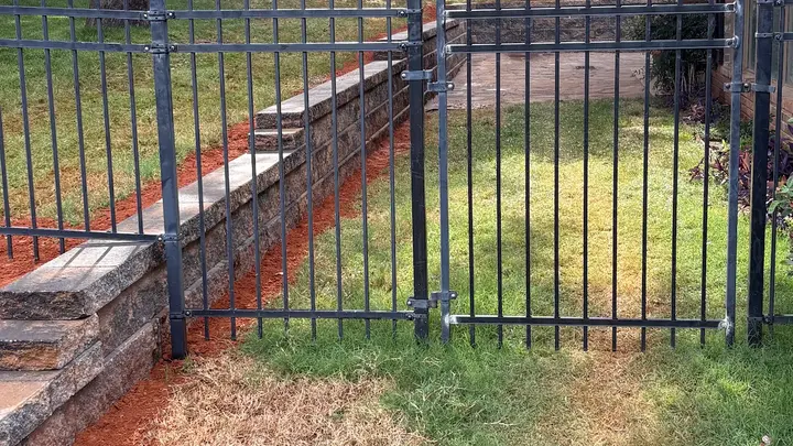 Retaining wall running along an iron fence line in a backyard