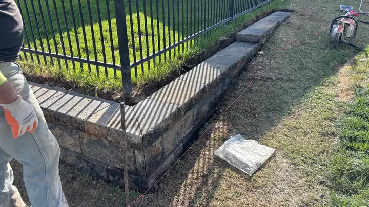 Crew finishing a low segmental block retaining wall along an iron fence line
