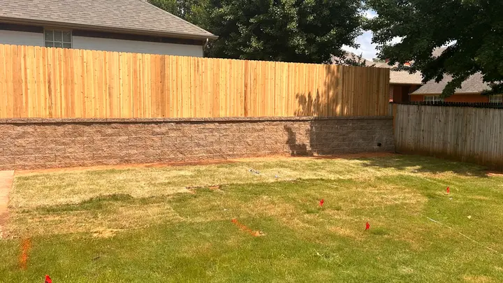 Tan block retaining wall with a new cedar fence built along the top