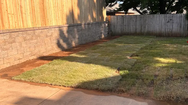 Block retaining wall supporting a fence line above a freshly sodded backyard