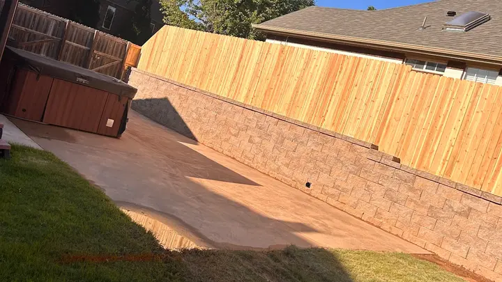 Long block retaining wall and cedar fence beside a backyard patio