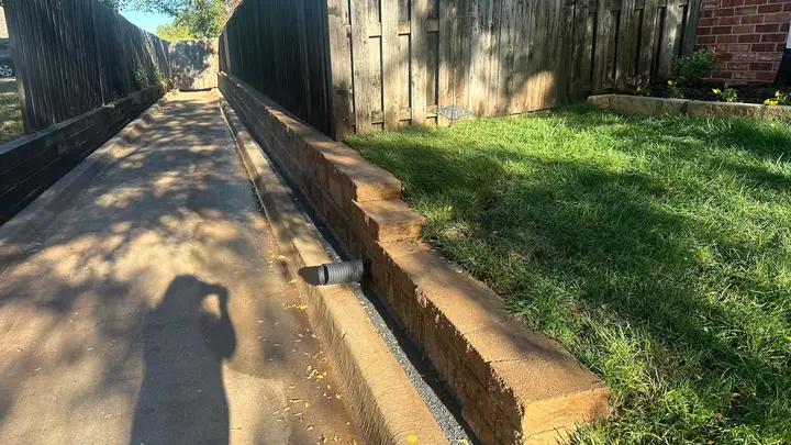 Low block retaining wall with drain tile daylighting beside a concrete drainage channel